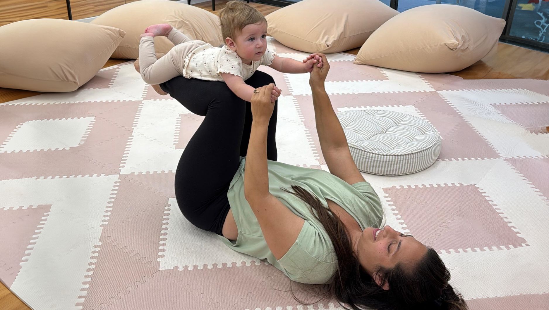 אמא שוכבת על מזרן ומחזיקה תינוק על הברכיים